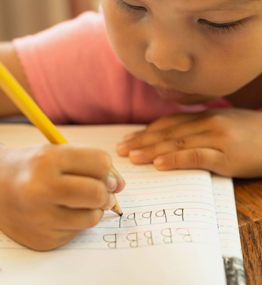 A young child learning how to write letters and alphabets, pencil and paper