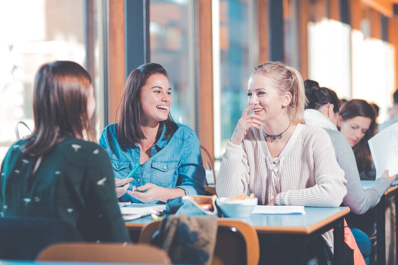 Drie studentes lachend aan een tafel