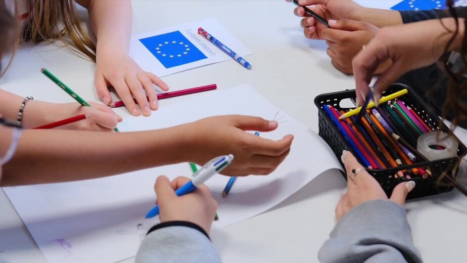 Pupils drawing together at a table, with a European flag on the worksheet